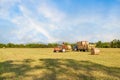 Agricultural scene. Tractor lifting hay bale on barrow.