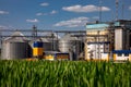 Agricultural Silos on the background of the field. Storage and drying of grains, wheat, corn, soy, sunflower against the blue sky Royalty Free Stock Photo