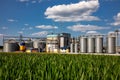Agricultural Silos on the background of the field. Storage and drying of grains, wheat, corn, soy, sunflower against the blue sky Royalty Free Stock Photo