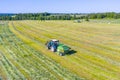 An agricultural tractor collects mowed grass for agricultural use and wraps hay bales in a plastic field, aerial view