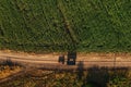 Agricultural tractor with empty wagon trailer on countryside dirt road in summer, casting shadow on the ground, aerial shot from