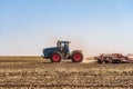 Agricultural tractor is working in the field under blue sky at daylight. Soil cultivation.