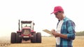 Agriculture. farmer working on a digital tablet in a field in the background a tractor plows ground in a field of wheat Royalty Free Stock Photo