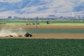 Agriculture tractor with plow in a fresh green field with mountains at background in California