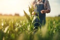 Agronomist farmer stands in a green field and examines immature green corn plants. Farmer inspects the crop. Generative AI