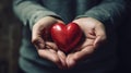 Close up of hands cradling a red heart, symbolizing love, care, and compassion, set against a soft-focused dark background