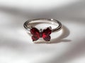 Elegant silver ring with a red butterfly gemstone on a soft white background Royalty Free Stock Photo