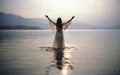 Baptism. Young woman in a long dress standing in the water with her hands raised