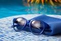 AI generated illustration of a pair of blue sunglasses rests on the edge of a swimming pool