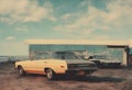 two parked cars in front of an old car with a building in the background