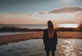 a person stands in the water by the shore looking at the sunset