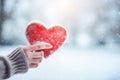 Female hand holding red heart shape in a winter landscape with snow