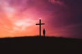 Silhouette of a man standing in front of a crossaSilhouette of woman standing at the cross over sunset sky background. Royalty Free Stock Photo