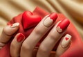 Matte red nails with small red heart on beige colour nail on the red fabric background. Saint Valentine\'s nail design