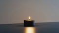 A small tealight candle with a flickering flame sits on a flat surface Royalty Free Stock Photo