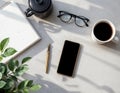 a smartphone, coffee, and a notebook on a desk with plants on foreground Royalty Free Stock Photo