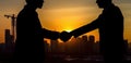 AI generative illustration showing the silhouette of two businessmen shaking hands, set against a vibrant sunset sky over a