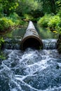 A serene creek receiving effluent from a drainage pipe, contrasting the natural beauty.