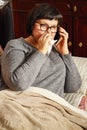 Ailing elderly woman on the couch talking on the phone and wipes her nose with a handkerchief. Royalty Free Stock Photo