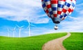 Air balloons flying in blue sky above green grass. Wind turbine in green hill.