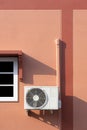 Air conditioner compressor with pipeline installation near white window on brown cement wall of vintage house