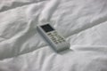 Air conditioner remote control on a bed with white sheets