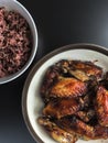 Air fried chicken wings on ceramic dish serve with small bowl of cooked Rice berry. All on black background. Royalty Free Stock Photo