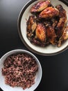 Air fried chicken wings on ceramic dish serve with small bowl of cooked Rice berry. All on black background. Royalty Free Stock Photo