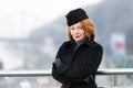 Air-hostess winter dress code. Woman standing near of bridge barrier in black coat. Portrait of lady with red hair crossing hands. Royalty Free Stock Photo