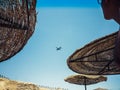 The air plane in the sky on the background of straw umbrellas on the beach in Sharm El Sheikh, Egypt Royalty Free Stock Photo