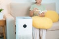 Air Purifier with woman read and relax on sofa. Purification system for filter and cleaning dust PM2.5 HEPA and virus in home.