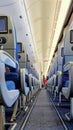 Aircraft cabin interior,airplane aisle,stewardess in red standing in distance,back view passenger seats,monitor screens Royalty Free Stock Photo