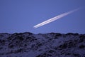 An aircraft flying in the blue sky very close to the mountain peaks. Passenger plane emitting smoke Royalty Free Stock Photo