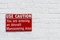 Aircraft manouvering red and white warning sign hung on painted brick wall.