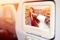 Monitor in front of passenger seat showing Happy women in blue dress with a shopping bag in shopping mall