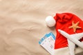 Airline tickets, Santa hat, toy airplane, starfish and space for text on beach sand, flat lay. Christmas vacation