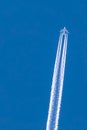 Airplane at cruising altitude seen from below with white contrails and a clear blue and cloudless sky Royalty Free Stock Photo