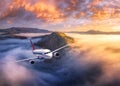 Airplane is flying above mountain peak in low clouds at sunrise Royalty Free Stock Photo