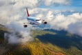 Airplane is flying in clouds over mountains with forest at sunse Royalty Free Stock Photo