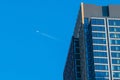 An airplane passes high above a tall New York City skyscraper with a glass and concrete facade Royalty Free Stock Photo