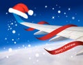 Airplane with red Santa Christmas hat over clouds and blue sky.