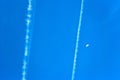 Airplane trails on a blue sky visible moon