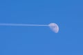 Airplane with white jet trail approaching the Moon with blue clear sky in background