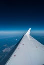 Airplane window view of blue sky and earth with visible white wing in frame Royalty Free Stock Photo