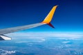 Airplane wing flying high in the atmosphere against the background of blue air. White-orange plane in the sky above the clouds and Royalty Free Stock Photo