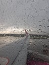 Airplane wing seen through a window covered with raindrops on a cloudy day - concept of fast travel