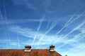 Airplanes tracks sprayed in the sky above a tiled roof.