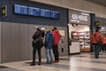 In the airport building, three male passengers in jackets and protective masks stand and watch attentively on the