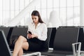 Airport woman on smart phone at gate waiting in terminal. Air travel concept with young casual business woman sitting