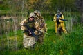 Airsoft players in uniform with weapons in their hands are walking in the forest